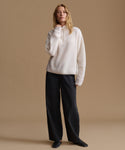 A woman modeling a cream ribbed knit half-zip sweater and black wide-leg trousers against a solid beige studio background.