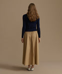Woman wearing a navy Cashmere Leni Crewneck and beige skirt against a brown background