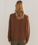 A person with long, wavy blonde hair is seen from behind, wearing the Cashmere Oversized Crewneck and olive green pants, standing against a plain light-colored background.
