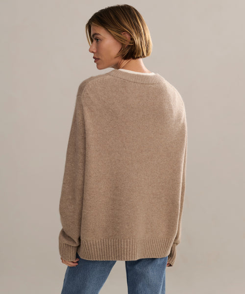 A woman with short brown hair wears a Cashmere Oversized Crewneck and blue jeans, standing against a plain, light background while looking to her left.