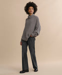 A person stands against a beige background wearing the Cashmere Porter Turtleneck, paired with dark jeans and black shoes. One hand is in their pocket as they look off to the side with a neutral expression.