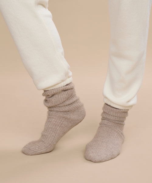 A person wearing off-white sweatpants and Cashmere Socks stands on a neutral beige background, one foot slightly raised.