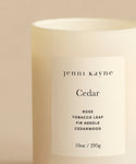 The Cedar Glass Candle from Jenni Kayne, a 10oz cream-colored candle hand-poured in Los Angeles, features rose, tobacco leaf, fir needle, and cedarwood notes. One of Oprah’s Favorite Things, it’s pictured against a neutral background.