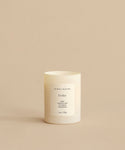 The Cedar Glass Candle, hand-poured in Los Angeles, features a minimalist white design and scent notes of rose, tobacco leaf, and cedarwood. It is shown on a beige surface with a matching beige background.