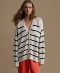 Woman wearing a white cardigan with black stripes and red pants on a beige background