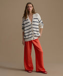 Woman wearing a striped cardigan and red pants against a beige background