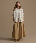 Woman wearing a striped cardigan and beige skirt against a brown background