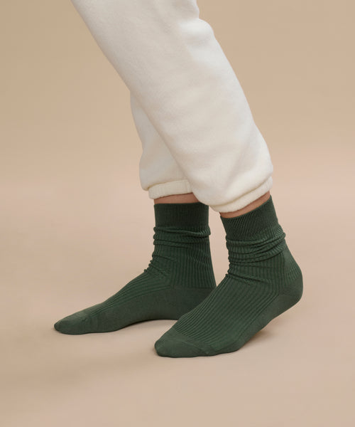 A person wearing cream-colored fleece pants and Classic Sock in dark green stands on a beige background.