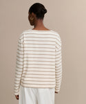 A person with hair in a neat bun wears the Claude Long-Sleeve Tee, featuring nautical stripes, and loose white pants while standing against a plain beige background, shown from the back.