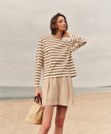 Woman in a striped shirt and shorts standing on a beach.