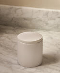 A Coast Canister in handcasted white resin with a round lid rests on a marble countertop and backsplash—an elegant touch to your home accessories collection.