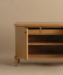 The Coast Sideboard is a Mid-Century Modern wooden sideboard with angled legs, two small drawers, and an open cabinet door showing two interior shelves, all displayed against a plain beige background.