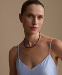 Woman wearing a lapis Constellation  necklace and light blue top against a beige background