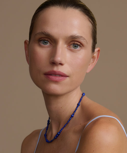 Woman wearing a lapis Constellation necklace against a brown background