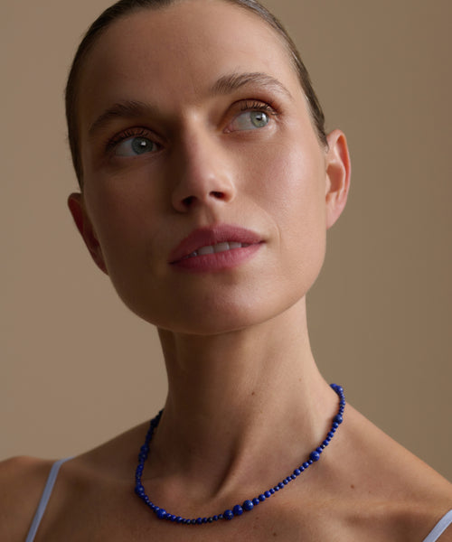 Woman wearing a lapis Constellation necklace against a beige background