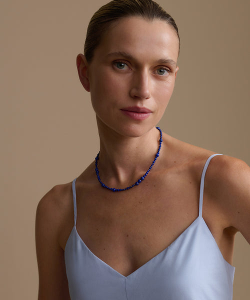 Woman wearing a lapis Constellation  necklace and light blue top against a beige background