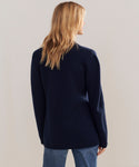 A woman with blonde hair wears the Cooper Blazer in dark navy and blue jeans, standing with her back to the camera against a plain light background.