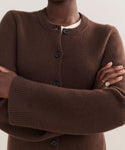 A person with crossed arms wears the Cooper Cardigan over a white top. The photo highlights only their torso and arms, showing the cardigan’s structured fit and a simple silver ring on one finger.