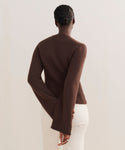 A person stands facing away, wearing the Cooper Cardigan in brown with a structured fit and off-white pants. Their hair is in a neat bun, one hand behind their back, against a plain, light-colored background.