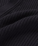 Close-up of the black Cotton Cocoon Cardigan shows ribbed, textured knitted fabric with visible stitches and soft folds, highlighting its detailed woven pattern crafted from organic cotton.