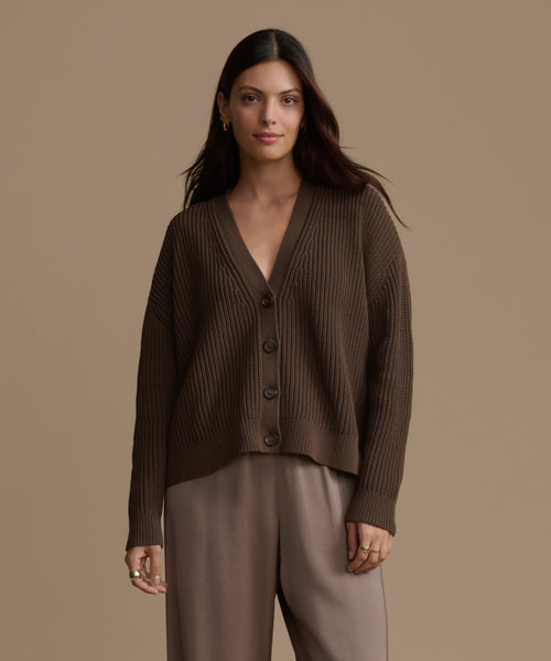 Woman wearing an olive cotton cropped cocoon cardigan and pants against a beige background