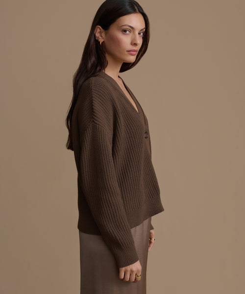 Woman wearing an olive cotton cropped cocoon cardigan against a beige background