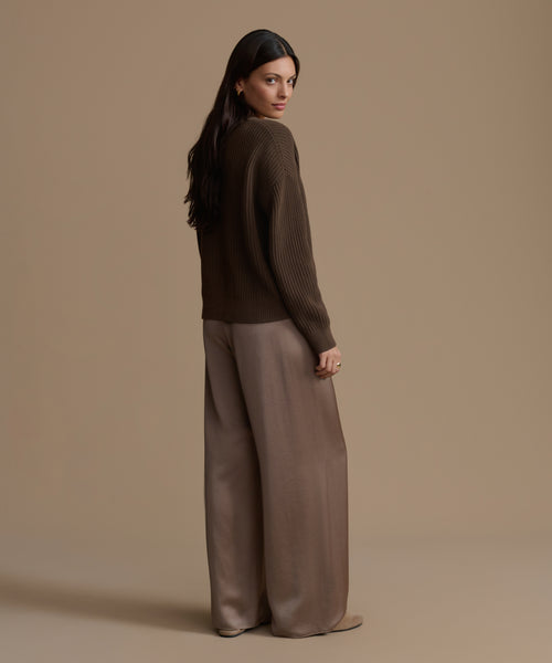 Woman wearing an olive cotton cropped cocoon cardigan and wide-leg pants against a beige background