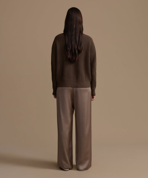 Person wearing an olive cotton cropped cocoon cardigan and wide-leg pants against a beige background