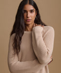 A woman wearing a beige ribbed knit sweater, posed against a solid beige background.