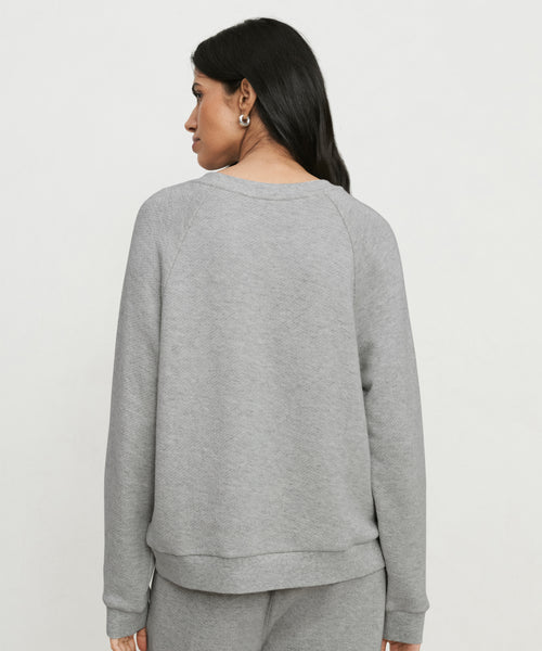 A woman with long dark hair, wearing the Saturday Sweatshirt and matching French terry pants, stands facing away from the camera against a plain light background.