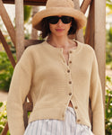 Woman wearing a beige knit cardigan, sunglasses, and a straw hat outdoors.