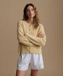 Woman wearing a light yellow sweater and white striped shorts against a brown background