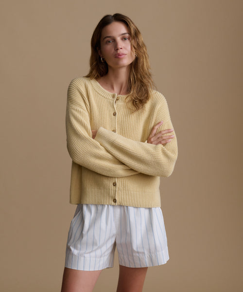 Woman wearing a light yellow sweater and white striped shorts against a brown background