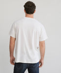 A man with short brown hair stands with his back to the camera, wearing a Mens Vintage Pocket Tee in ivory and dark blue jeans against a plain light background.