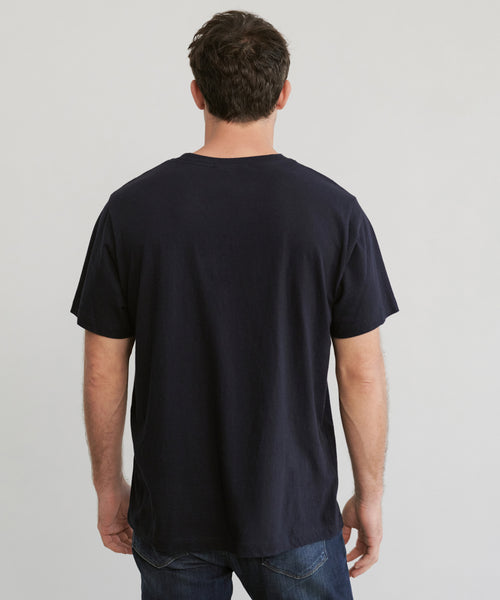 A man with short brown hair stands with his back to the camera, wearing the Mens Vintage Pocket Tee in plain black and blue jeans against a light gray background.