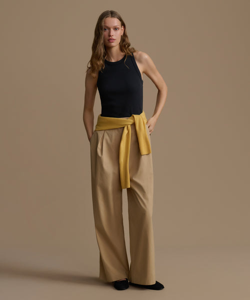 Woman wearing a black top and beige pants with a yellow belt against a brown background