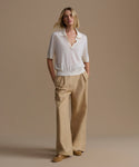 Woman wearing a ivory courtney top and beige pants against a beige background