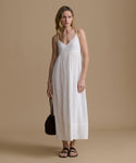 Woman wearing a white dress holding a black bag against a beige background
