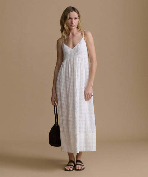 Woman wearing a white dress holding a black bag against a beige background