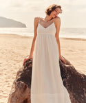 Woman in a white dress standing on a beach with a rock.