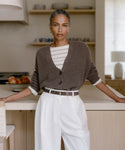 A woman stands in a kitchen wearing the Cropped Cashmere Cocoon Cardigan, effortlessly elevating her everyday look with this versatile piece.