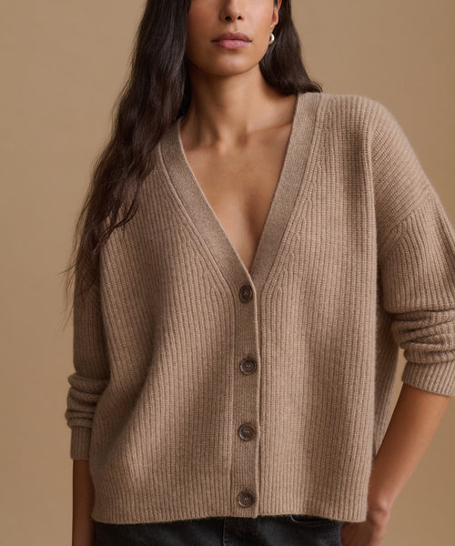 A woman wearing a taupe ribbed knit button-front cardigan sweater against a solid beige background.