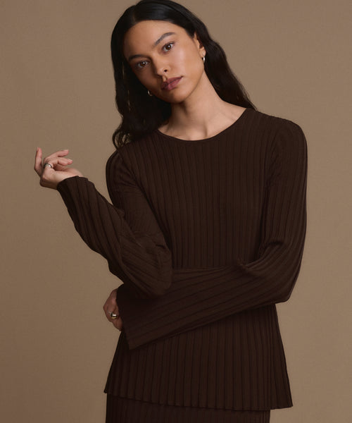 A woman with long dark hair wears the Dara Top in dark brown, standing against a plain brown background. She gazes forward with a neutral expression and has one hand slightly raised.
