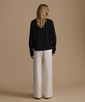 Woman wearing a black sweater and beige pants against a brown background