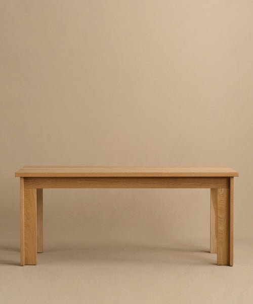 The Dining Table is handmade from solid white oak, featuring a rectangular top and four sturdy legs, displayed against a plain beige background.