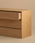 The Dune Dresser, a simple and modern light oak piece, features three drawers. Displayed against a neutral backdrop, its top drawer is slightly open, showcasing the interior—a perfect example of white oak furniture.