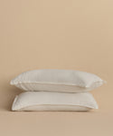 Two white pillows with Dusk Linen Pillow Sham Set of 2, stacked against a plain beige background.