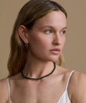 Woman wearing a green beaded necklace and green earrings against a beige background