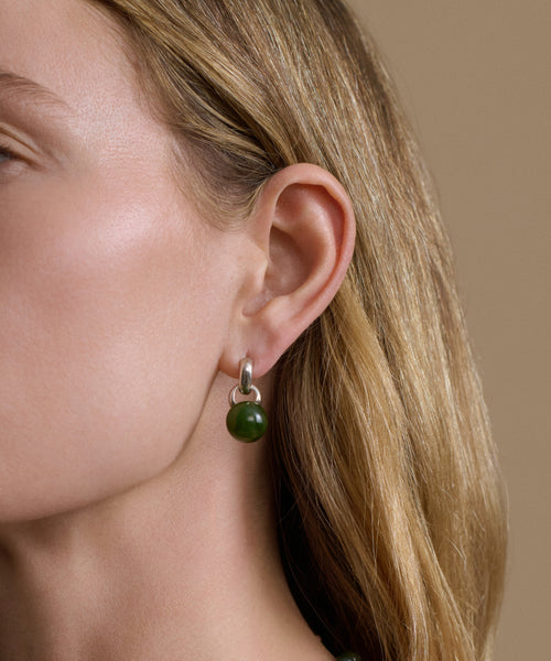 Close-up of a woman wearing a green bead earring with a beige background