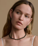 Woman wearing a green beaded necklace and earrings against a beige background